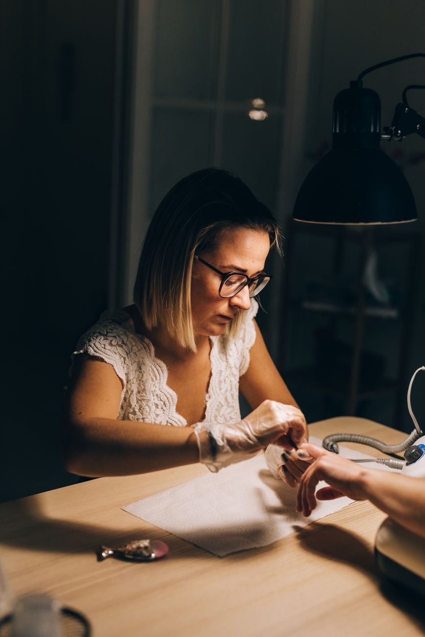 Woman providing a manicure under warm lighting in an intimate nail salon setting.